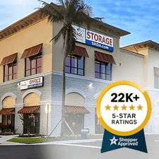 Exterior view of a Storage Rentals of America facility featuring palm trees, clear blue sky, and a badge showing Shopper Approved badge.