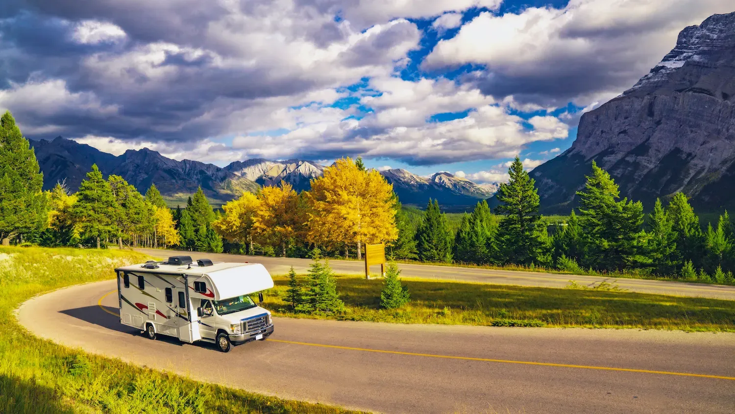 An RV on the road, driving on a clear day with Autumn trees.
