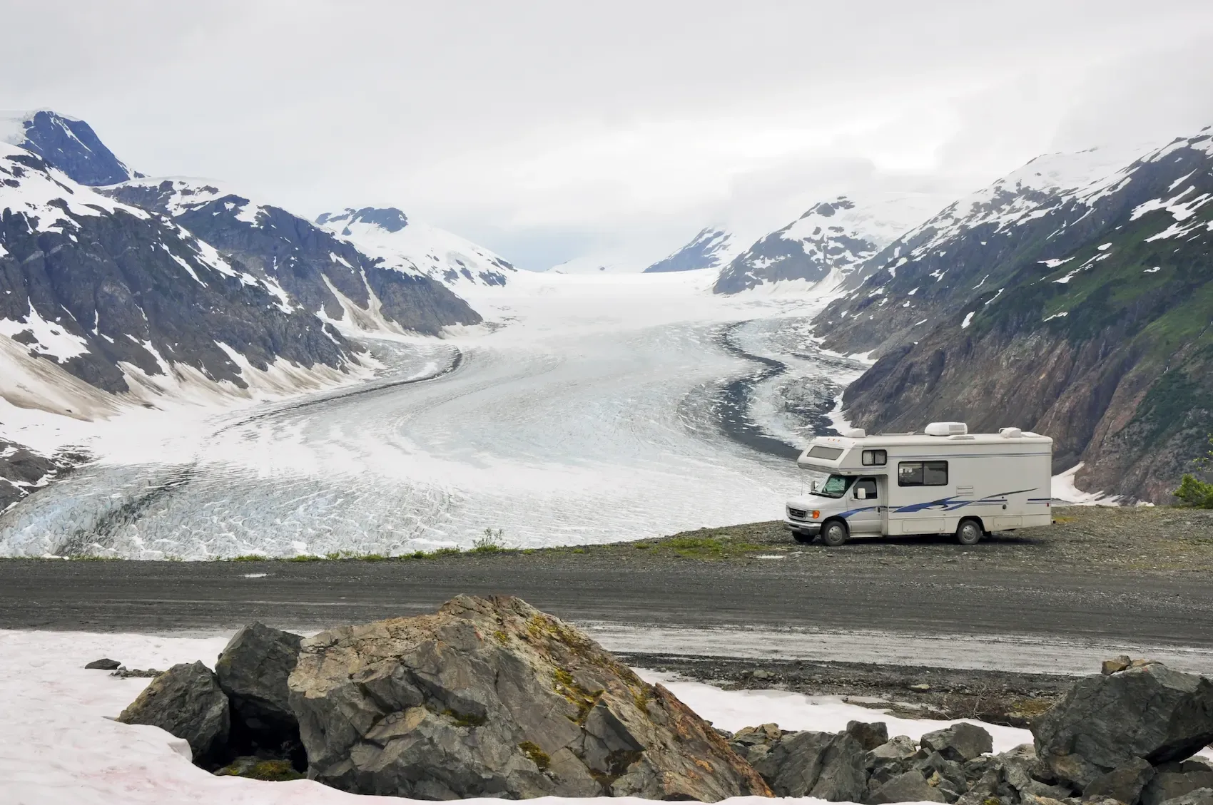 RV driving on the road during winter with snowy mountains in the background.