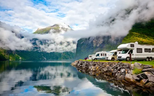 RVs parked outside in nature with the water and mountains in the background.
